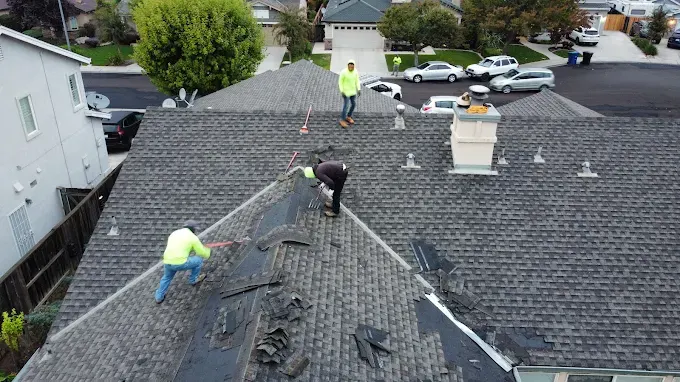 Repaired storm-damaged asphalt shingle roof on a modern suburban home in Modesto California with lush lawns and clear sky