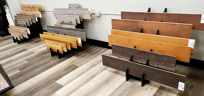 A flooring store displays numerous wood and laminate plank samples in various shades, from light to dark, on floor and wall stands.