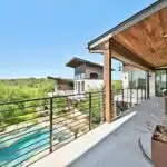 Beautiful completed covered patio in Austin TX with wooden pergola, tiled roof, lush greenery, outdoor furniture, and decorative lighting