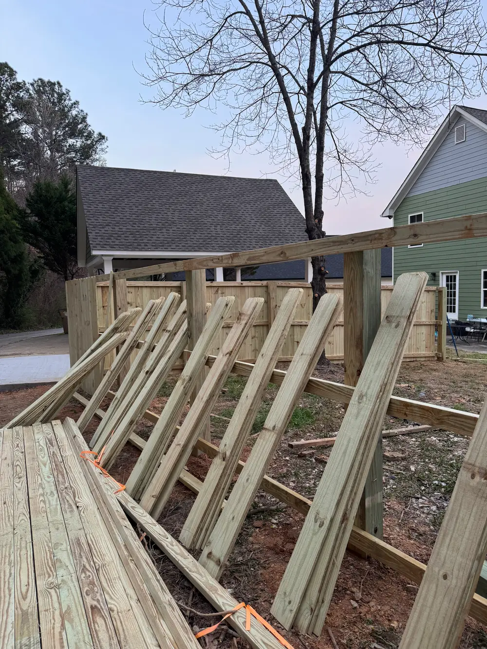 Wooden fence installation in Jacksonville AL with rich tones, neat panels, lush lawn, flowers, and sunny sky.