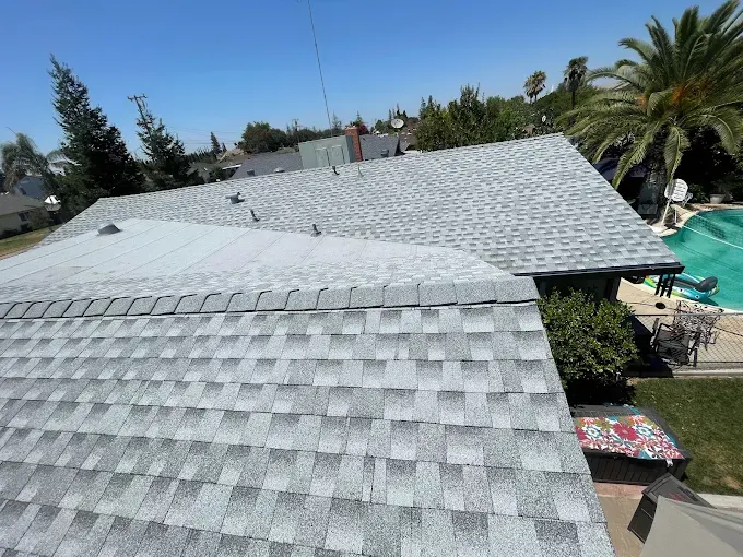 Recently repaired home roof in Modesto with new asphalt shingles, lush yard, mature trees, blue sky, and sunlight