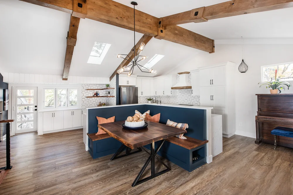 Bright, modern kitchen with vaulted ceiling, exposed wood beams, white cabinets, patterned backsplash, and navy blue dining nook.