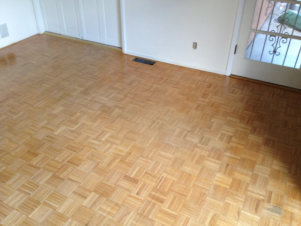 Clean, empty room showcasing light-colored, reflective parquet hardwood flooring, white walls, and a glass-paned door.