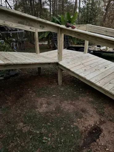 Newly built pressure-treated wooden wheelchair ramp and platform in a dirt backyard with a drill on the railing.
