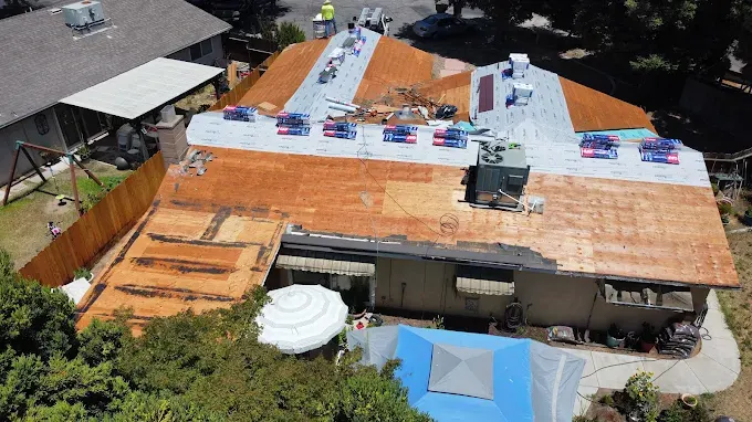 Close-up of a seamless ridge vent installation on a residential asphalt shingle roof in Modesto California with lush greenery in background