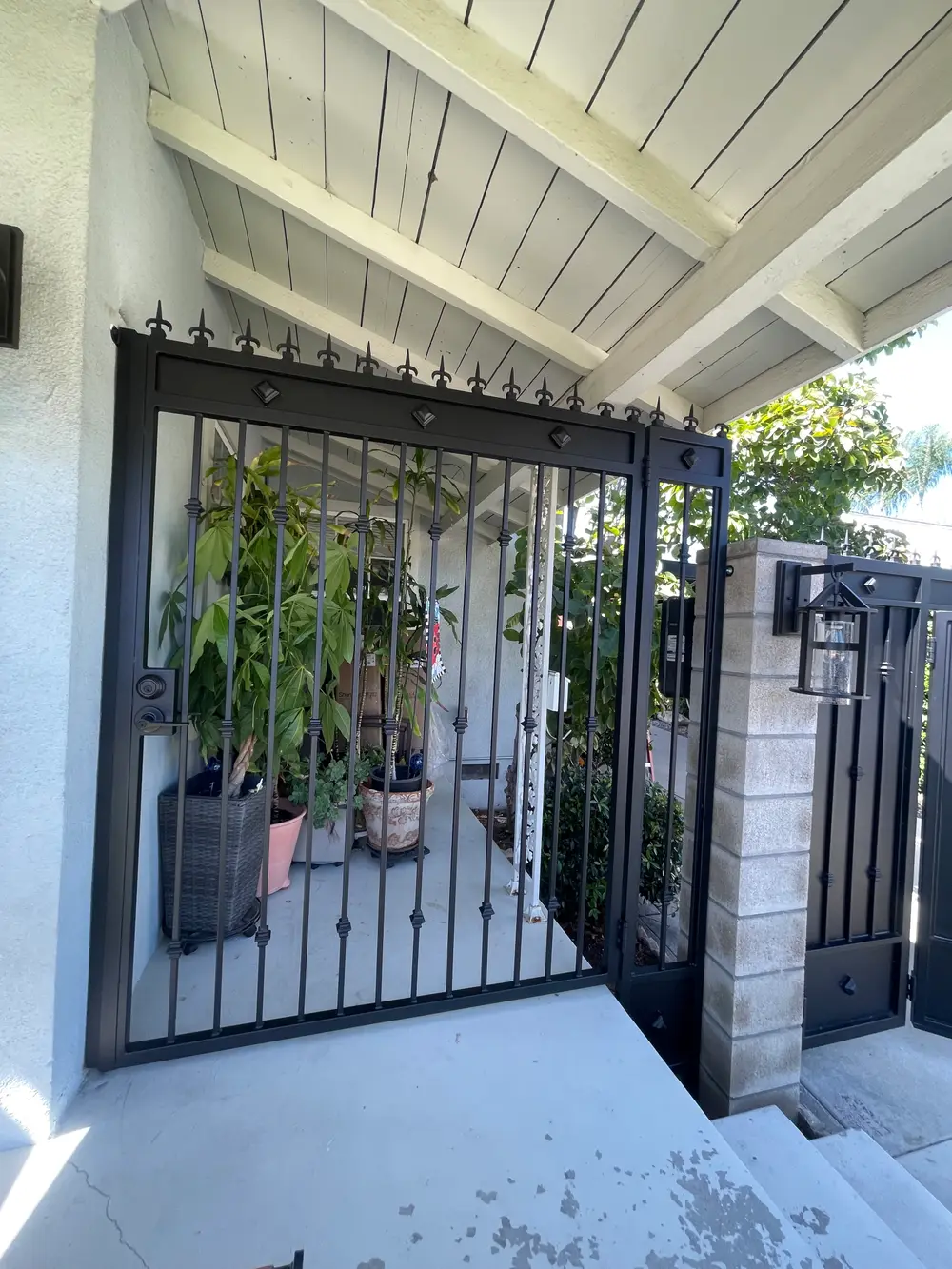Custom wrought iron gates in Los Angeles framed by lush greenery and vibrant flowers under a clear blue sky.