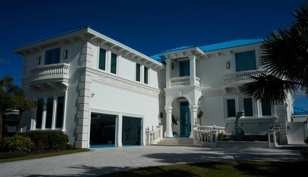 Exterior trim painting of a coastal house in New Smyrna Beach with white trim, tropical landscaping, and a clear sky.