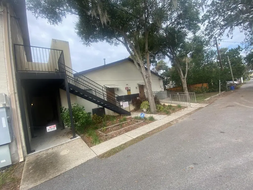 Charming coastal home in New Smyrna Beach with soft blue siding, white railings, and vibrant flowers under a clear sky.
