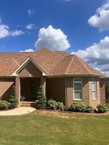 Newly installed asphalt shingle roof on a suburban home in Trussville AL with landscaped gardens and blue sky background.