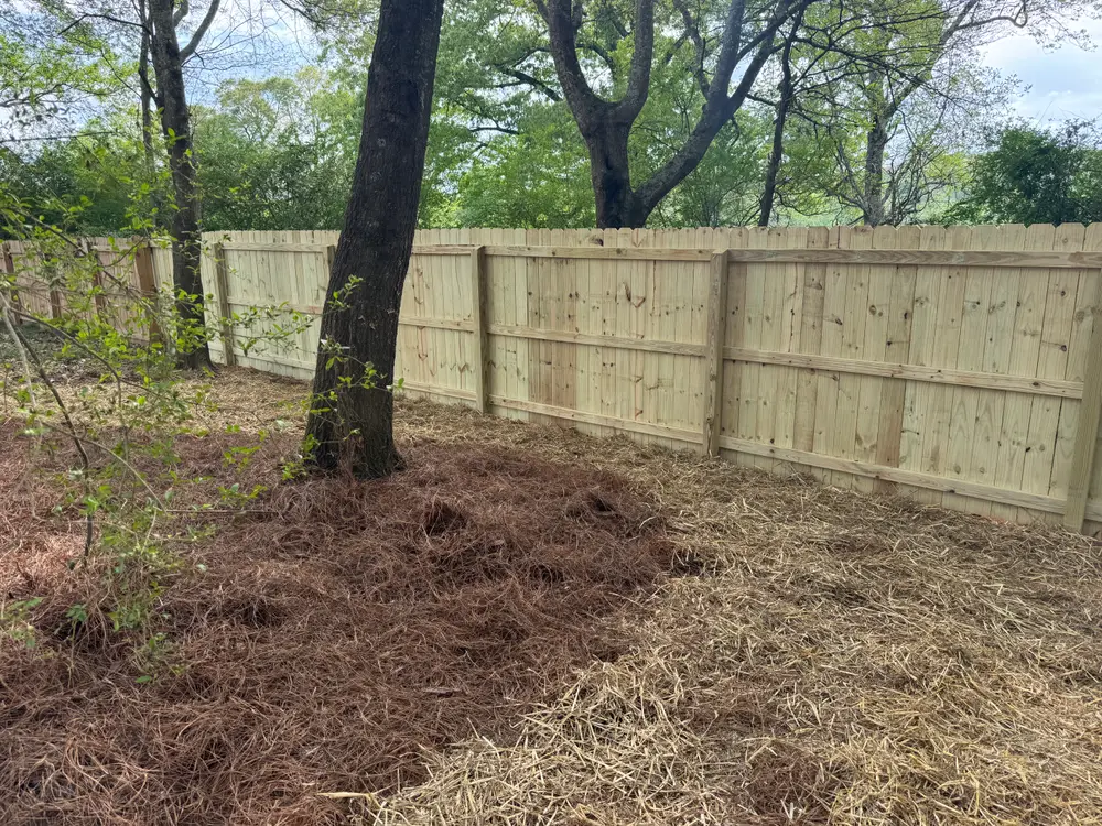 Completed wooden fence installation in Calhoun GA, surrounded by green grass and colorful flowers under a blue sky.