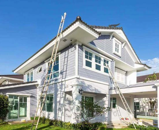A two-story house with blue siding and white trim features two ladders leaning against it, suggesting home maintenance or painting work.