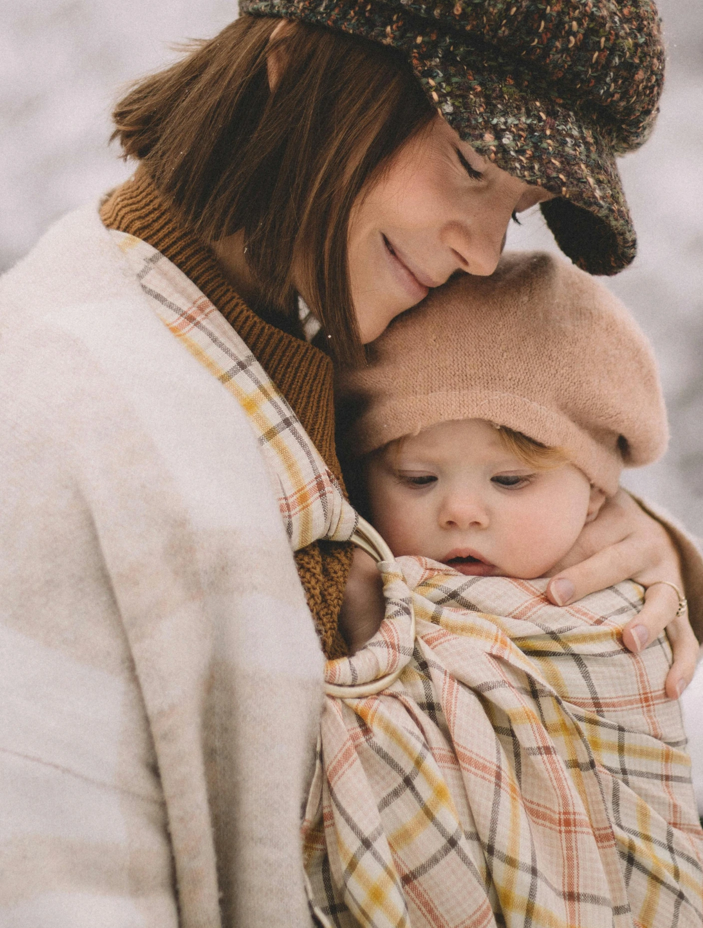 Une mère porte son enfant emmitouflé en écharpe l'hiver