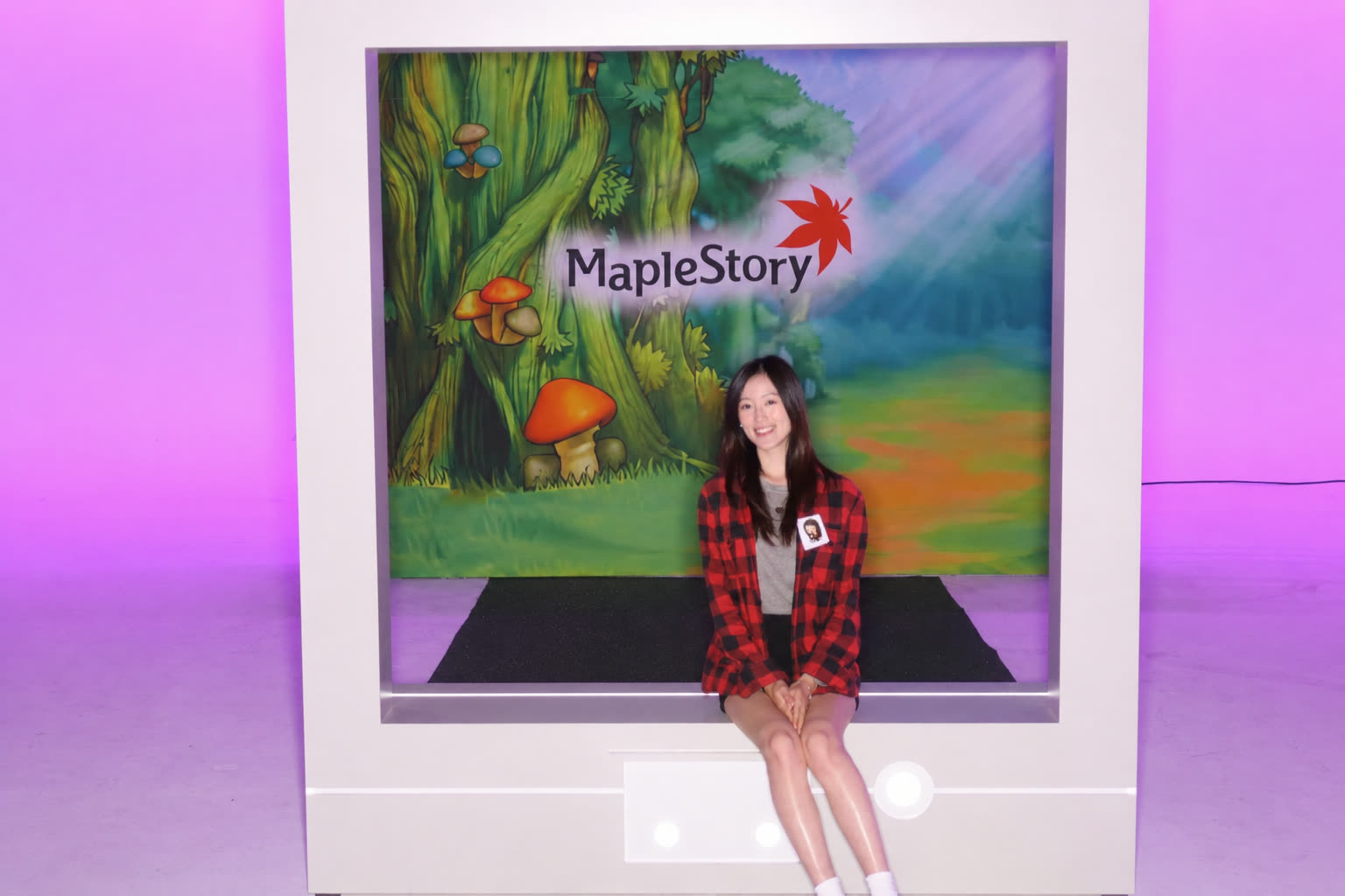 Fionn smiling in a red plaid shirt in front of a MapleStory backdrop