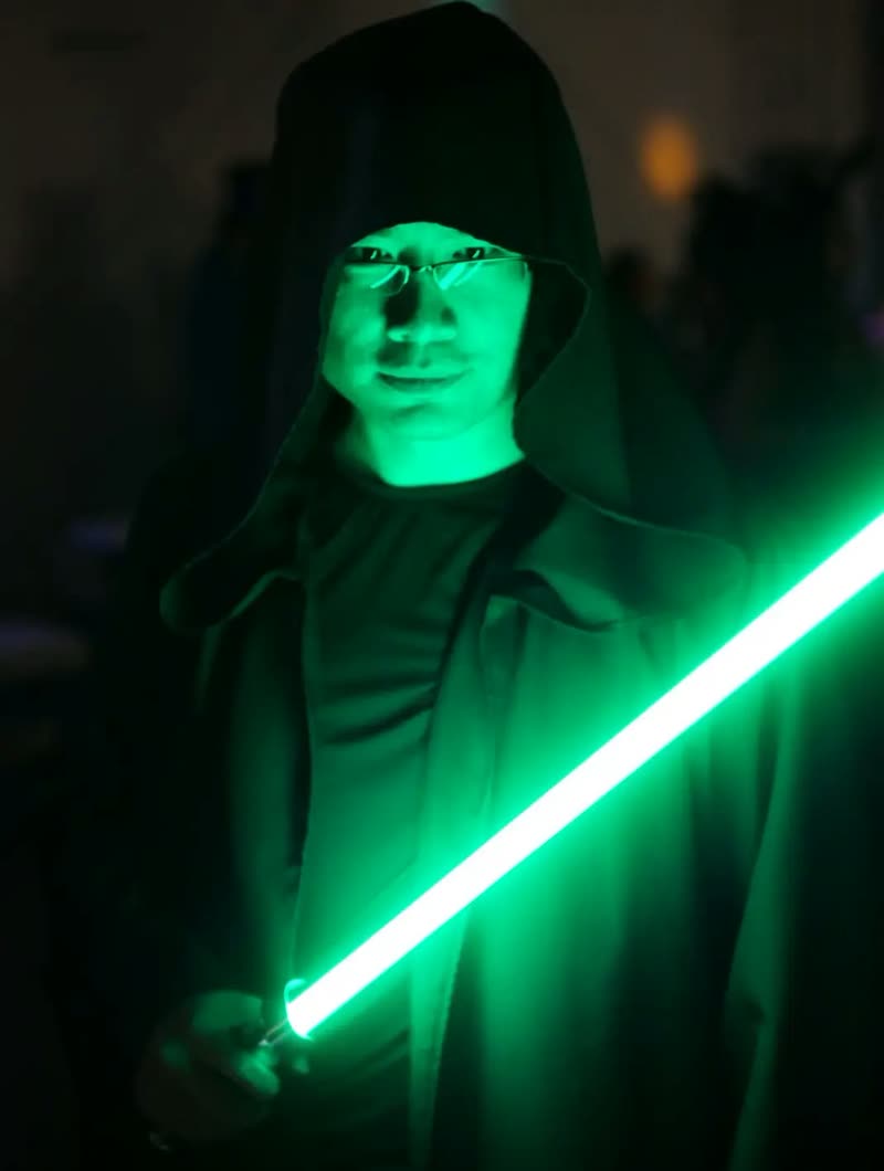 Lee Yu in a dark costume holding a glowing green lightsaber