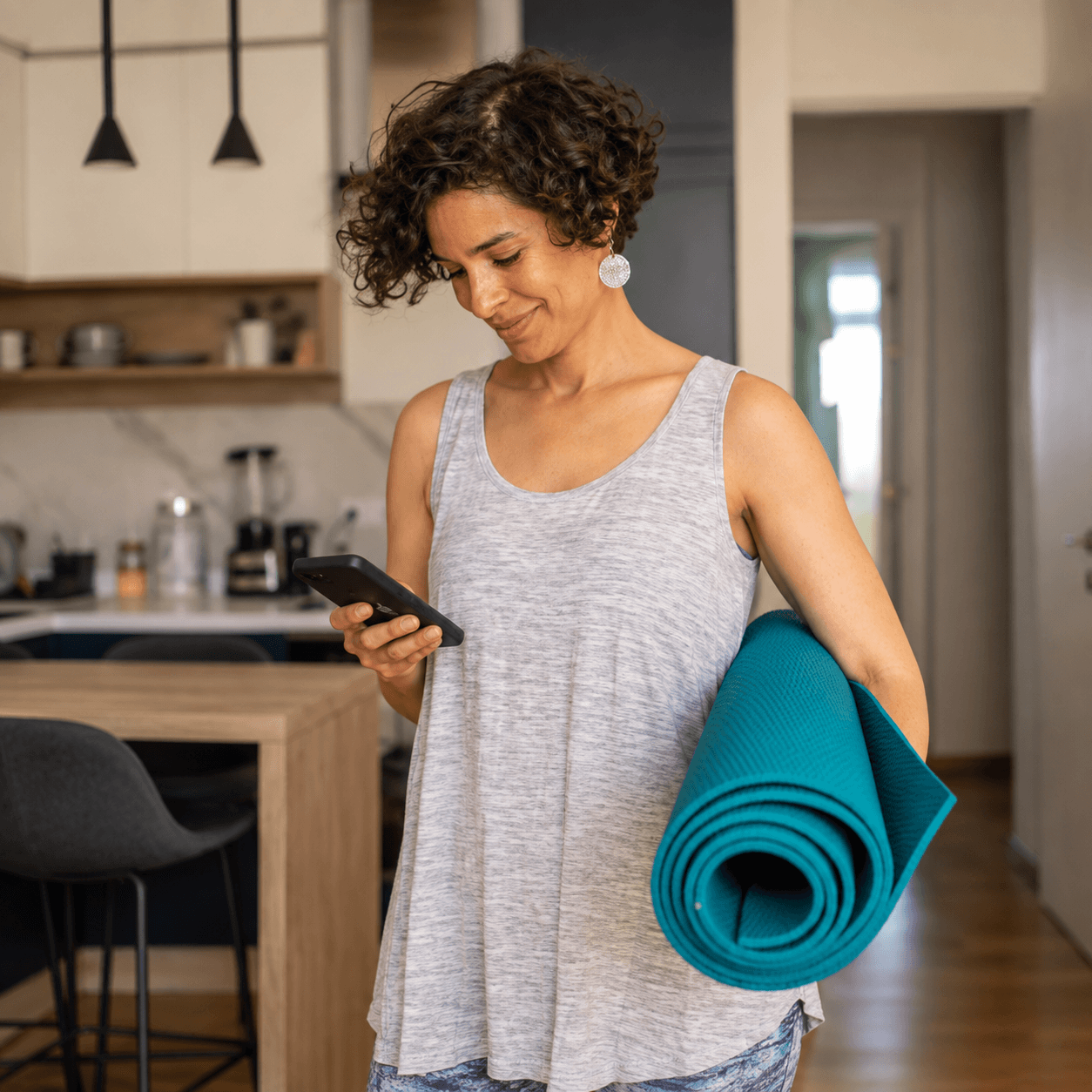 Woman holding a yoga mat and checking her phone at home as part of a healthy lifestyle routine.