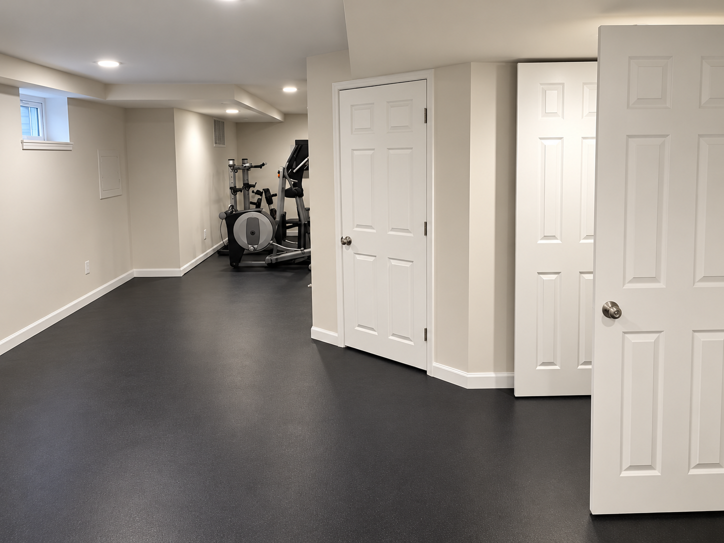 Finished basement with dark moisture-resistant flooring and home gym area by KingStruction