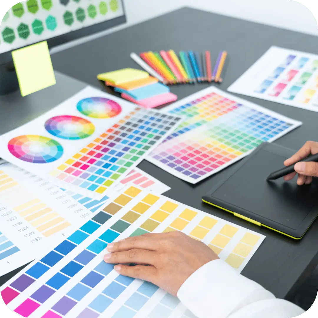 Pult dekket med fargeprøver, penner, notatblokker, nettbrett og skjerm for grafisk design