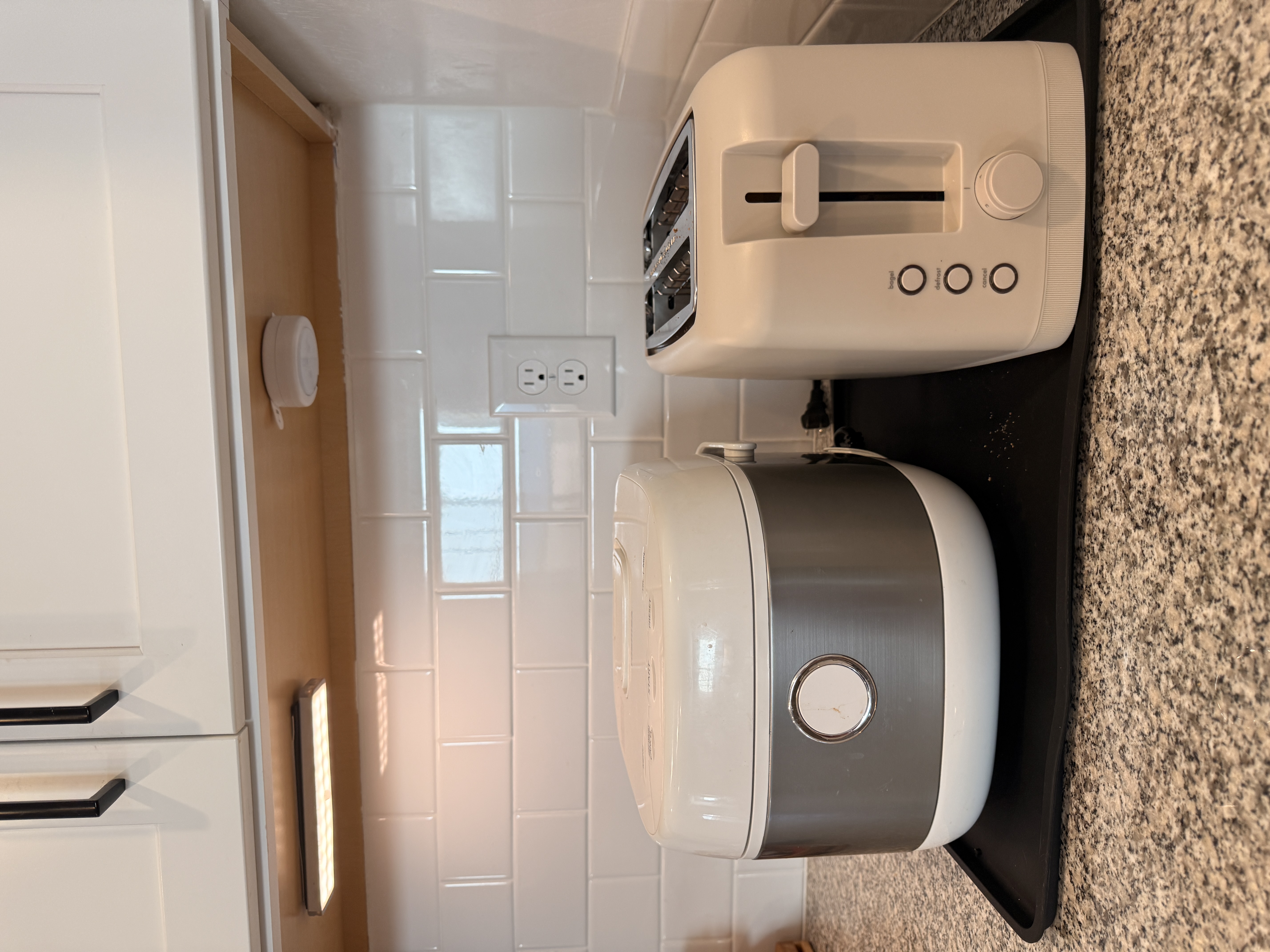 Rice cooker and toaster on a black countertop tray beneath an illuminated cabinet. Rice cooker and toaster on a black countertop tray beneath an illuminated cabinet.
