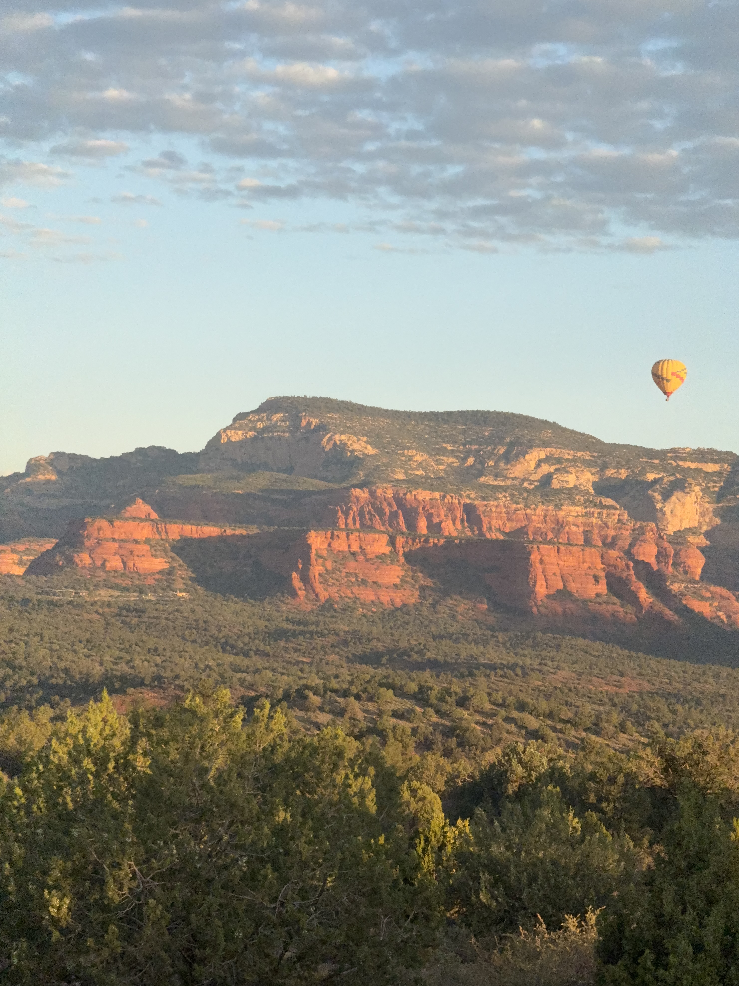 Golden sunrise light on the high red rock ridges near Cultural Park Trailhead in Sedona, Arizona, with a hot air balloon in the sky Golden sunrise light on the high red rock ridges near Cultural Park Trailhead in Sedona, Arizona, with a hot air balloon in the sky