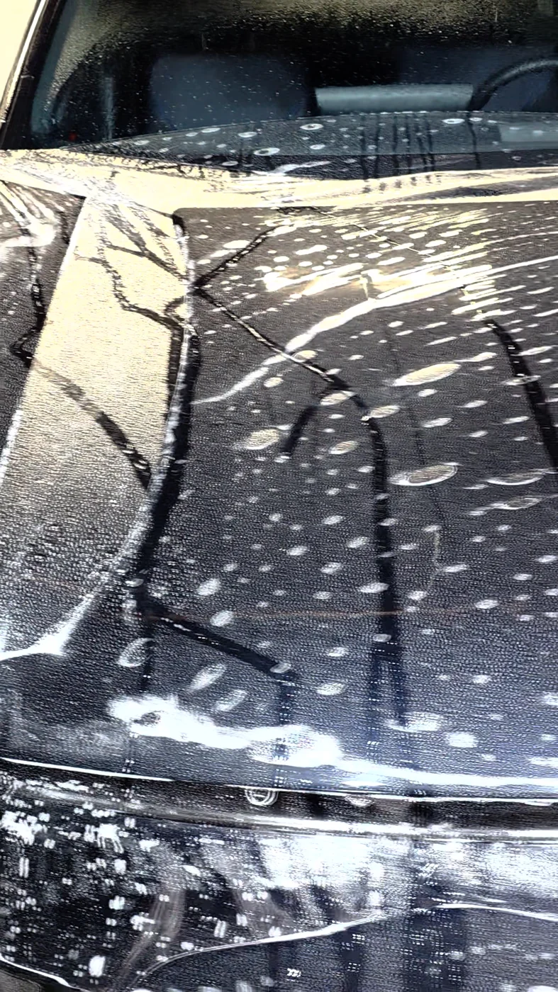 Clear paint protection film laid over the wet hood of a dark blue Toyota RAV4.