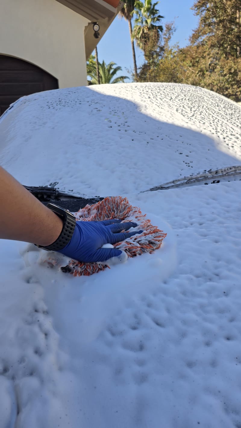 A gloved hand using a wash mitt on the foam-covered hood of the Acura NSX.