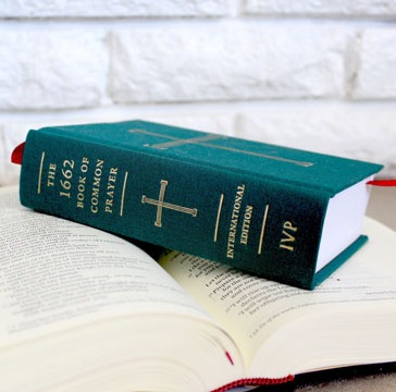 An open Book of Common Prayer and Bible resting on a table