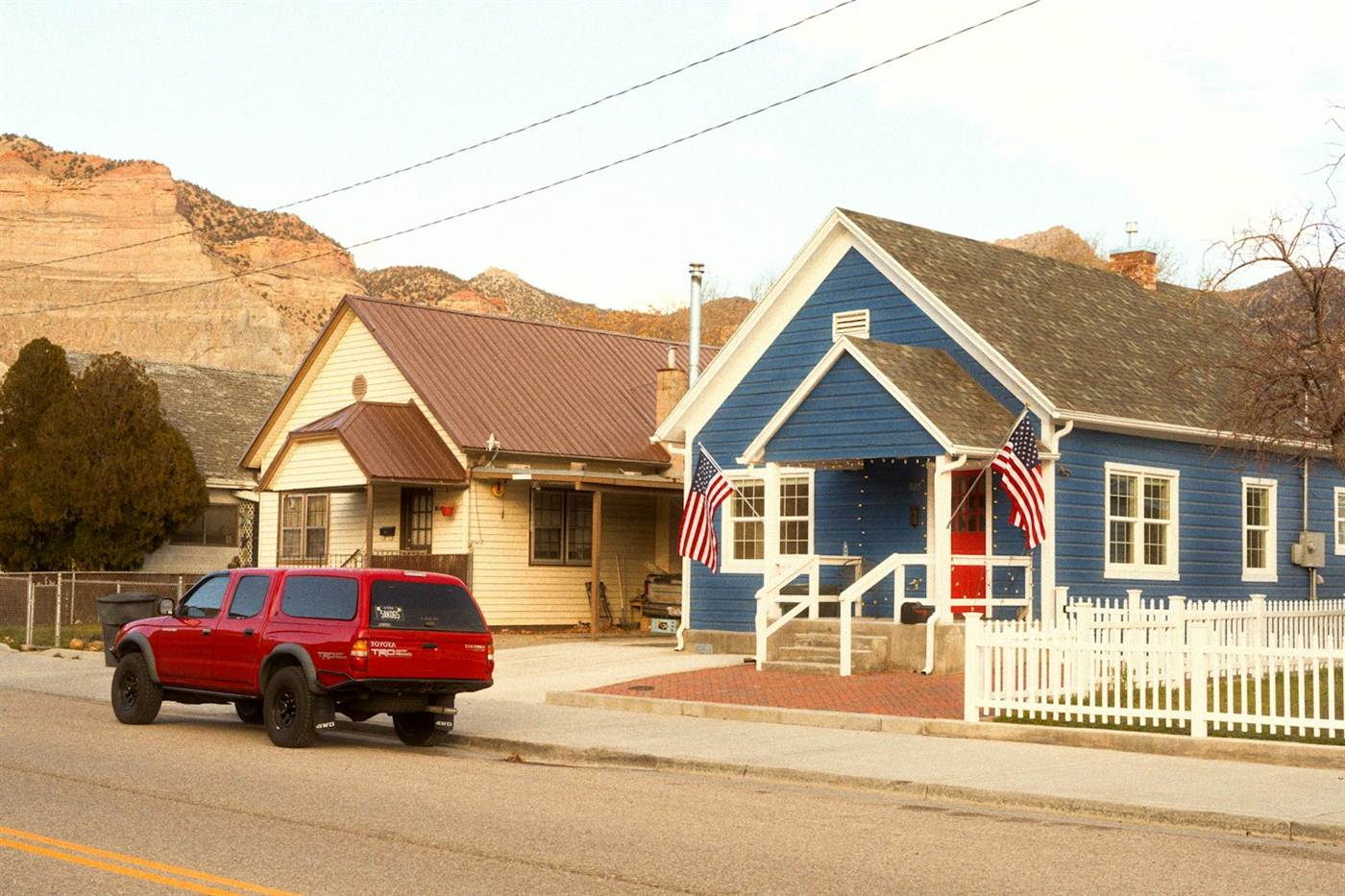 A small-town residential street in Utah with red rock mesas behind.