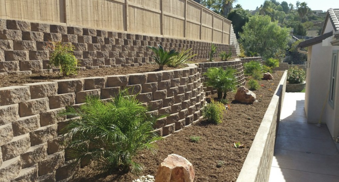 Tiered stone retaining walls along a sloped side yard with new planting and mulch