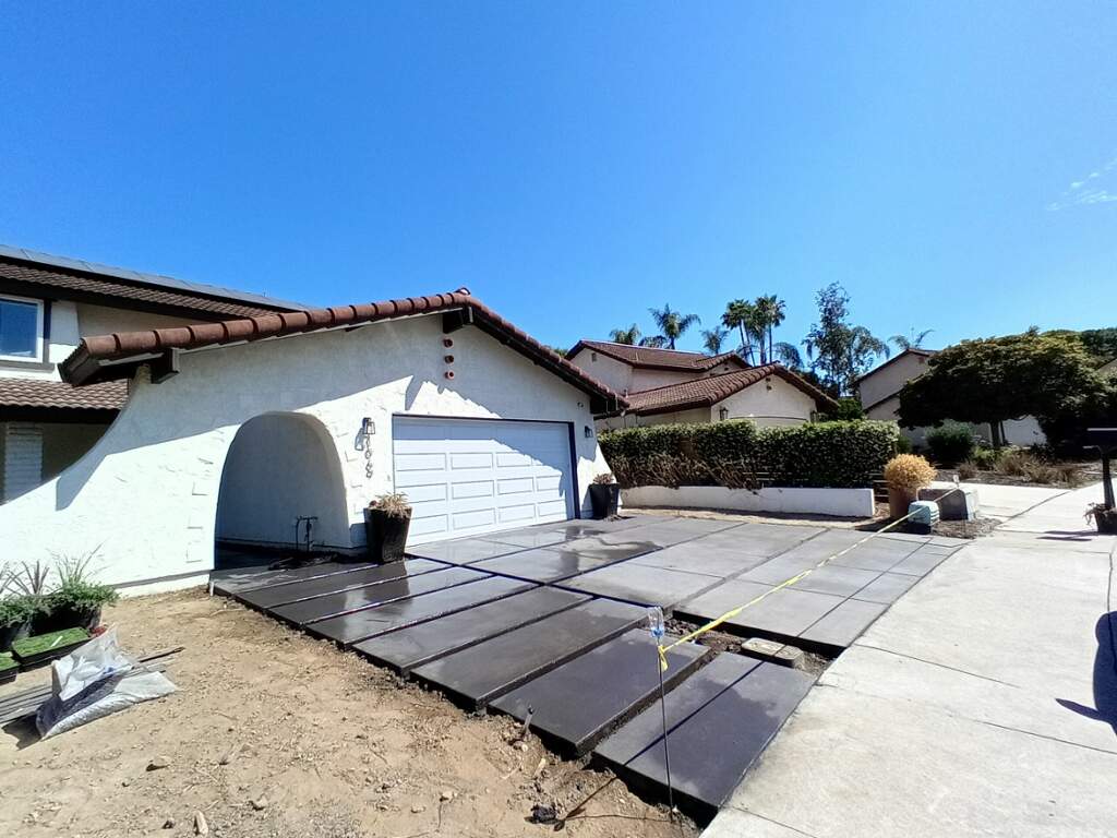 Dark stained concrete driveway slabs being installed in front of a Spanish-tile roof home