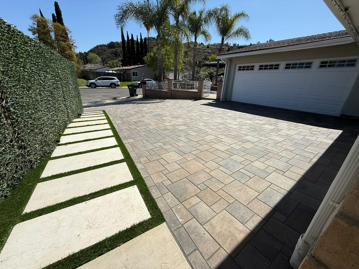Large interlocking paver driveway with artificial turf walkway leading to a two-car garage