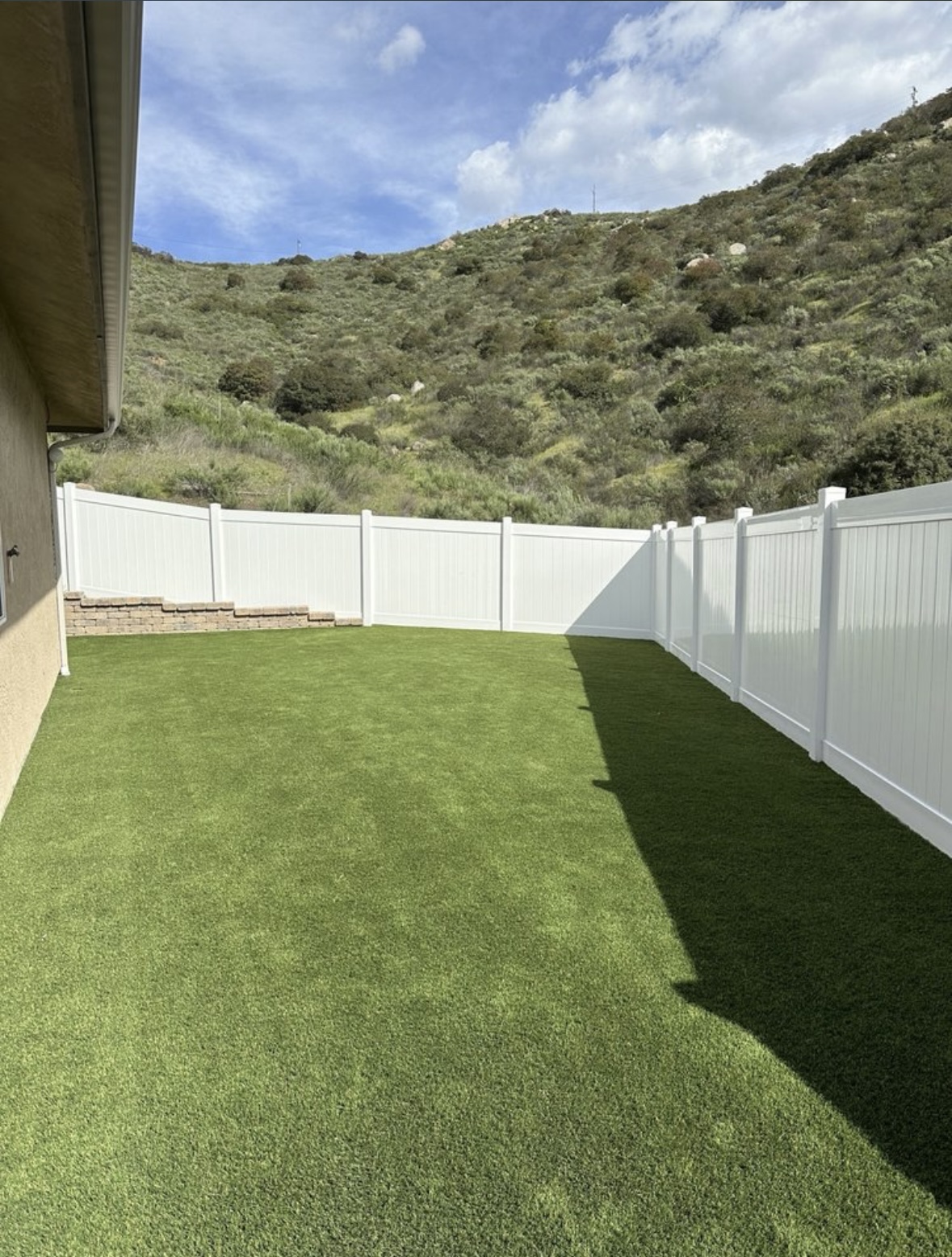 Backyard artificial turf with curved white vinyl fence and hillside view