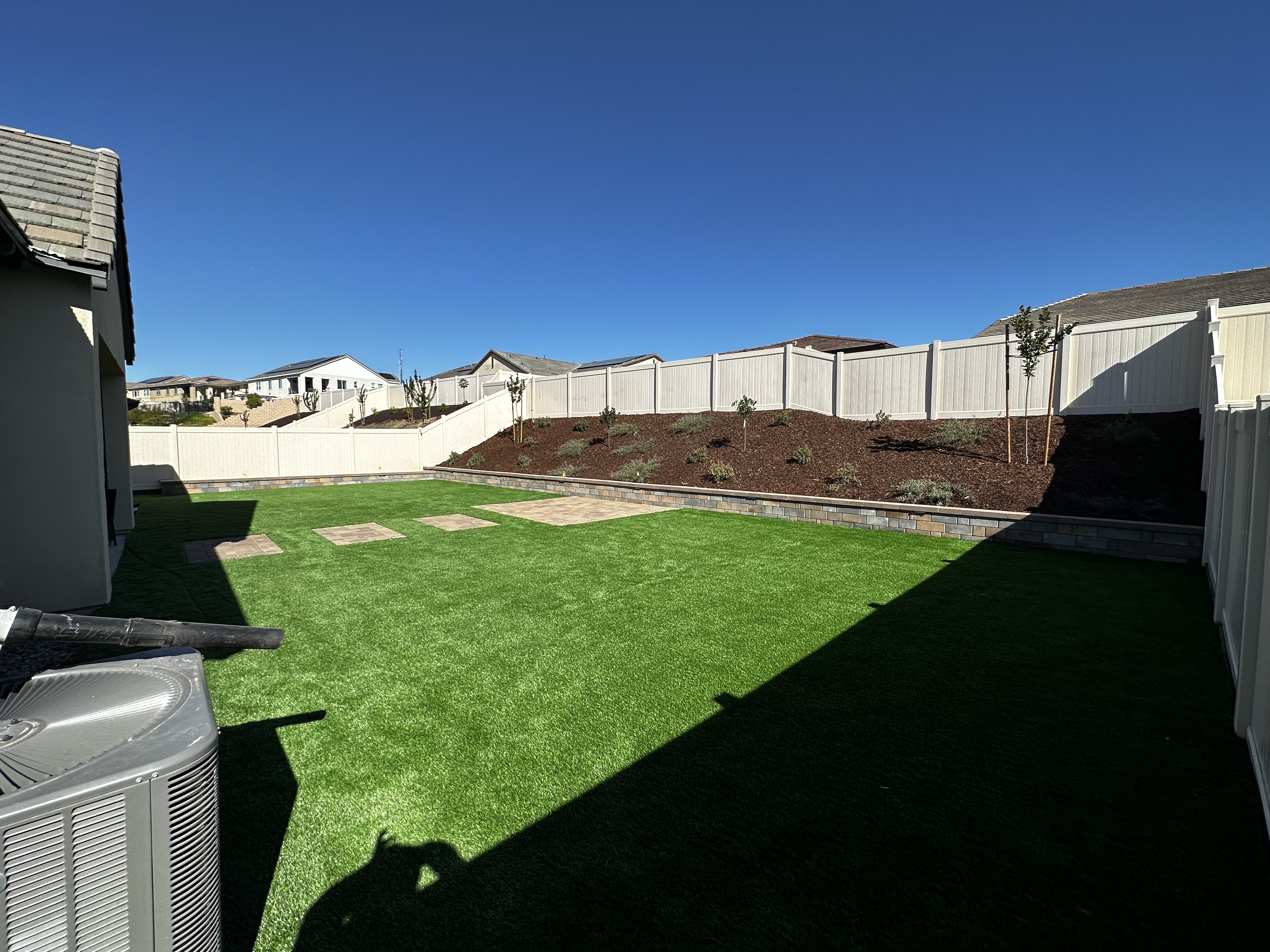 Sloped backyard with turf, stacked block retaining wall, and fresh planting bed