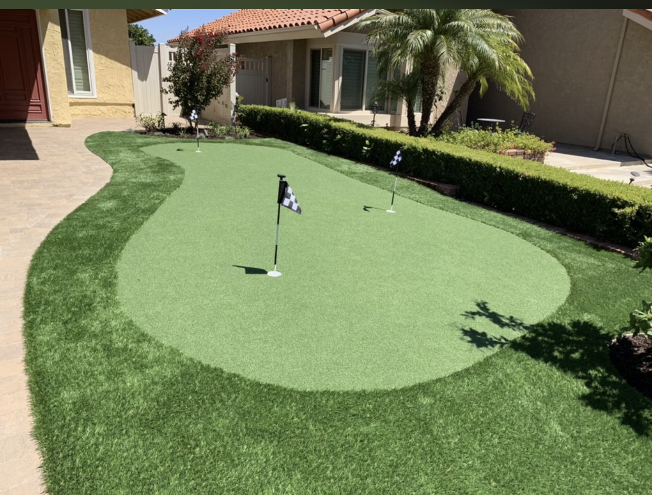 Front yard synthetic putting green bordered by hedges and paver patio