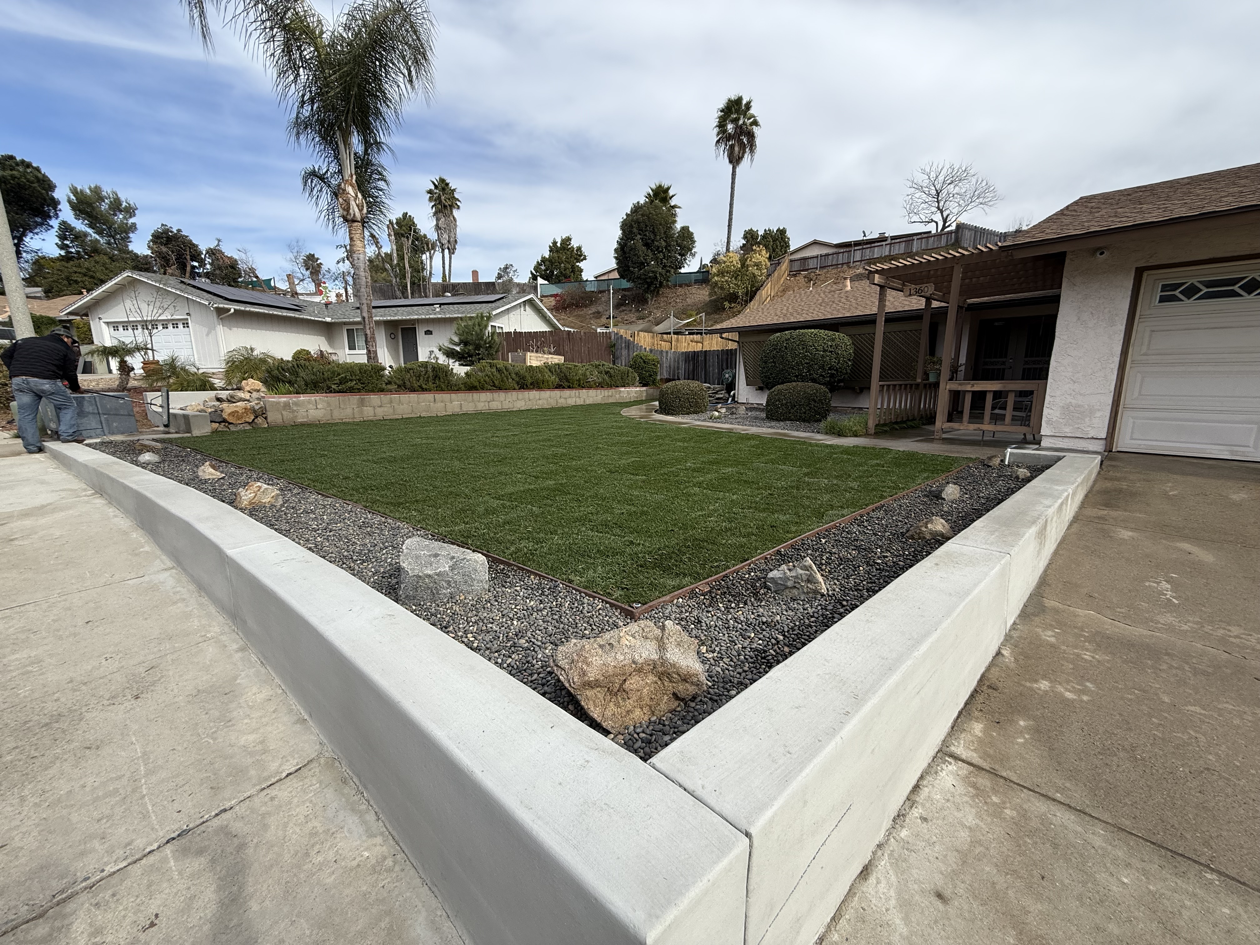 Front yard artificial turf with concrete border, decorative gravel, and boulder accents