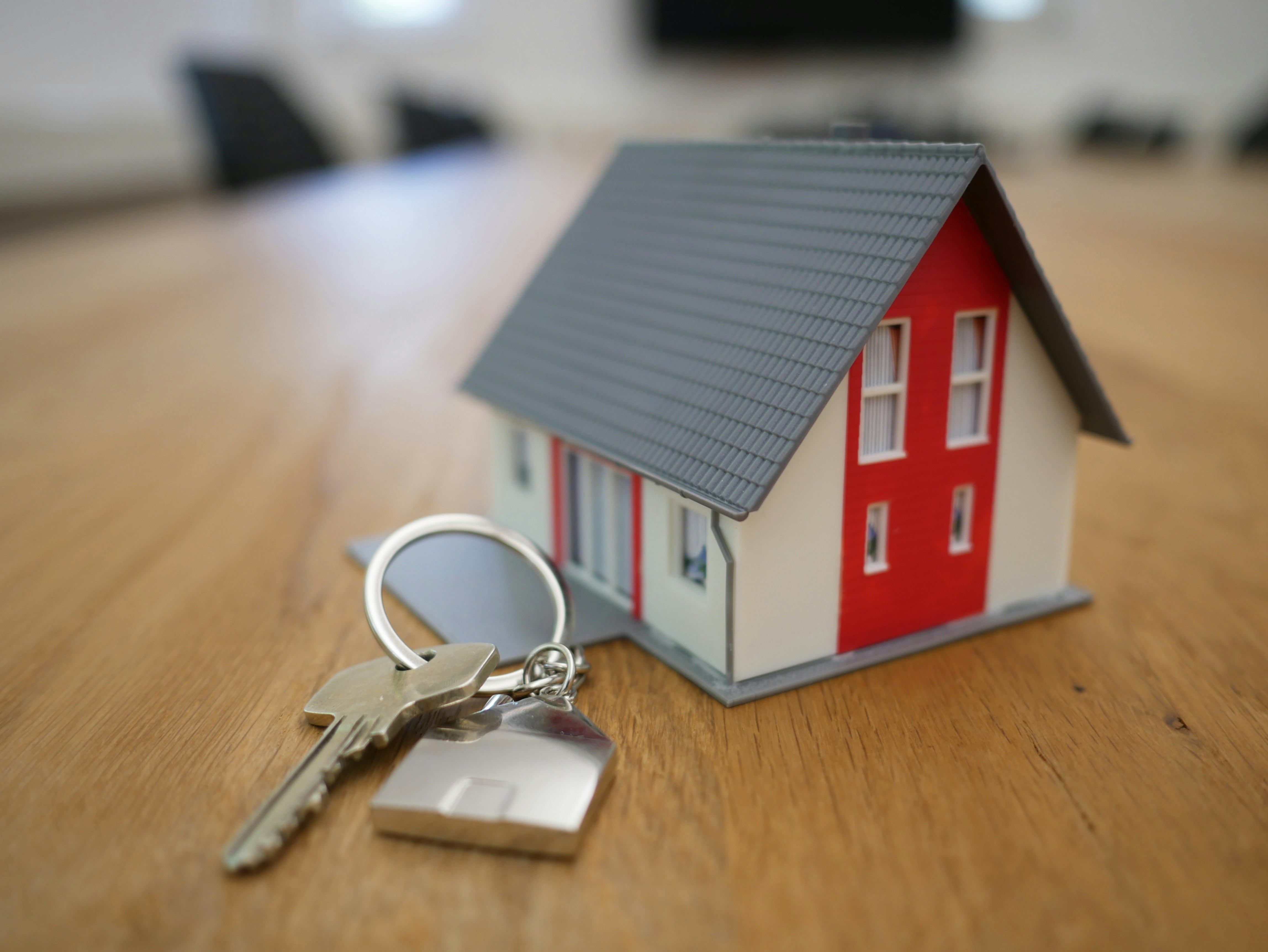 House keys with a house-shaped keychain sitting on a wooden table next to a small model house, representing real estate Cary North Carolina.