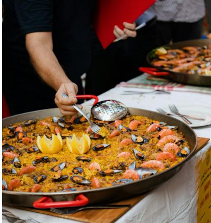Paella being served in large pan with seafood and lemon wedges Paella being served in large pan with seafood and lemon wedges