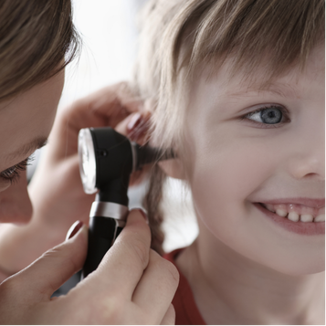 Smiling child receiving a gentle pediatric ear examination with an otoscope.
