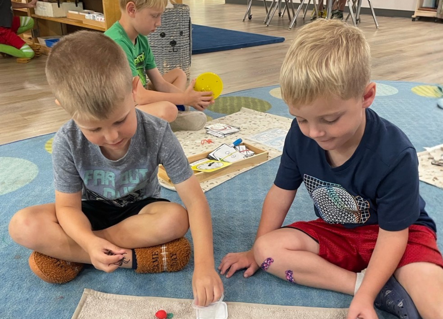Two Spark learners working with materials on a rug