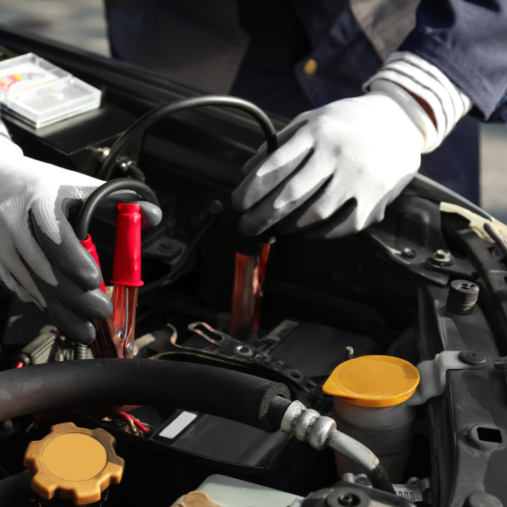 Mechanic using jumper cables to jump-start a vehicle’s engine.