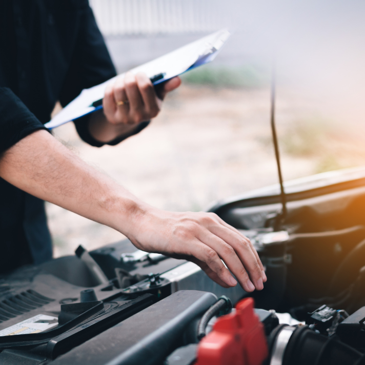 Technician performing a vehicle inspection with a clipboard, checking under the hood.