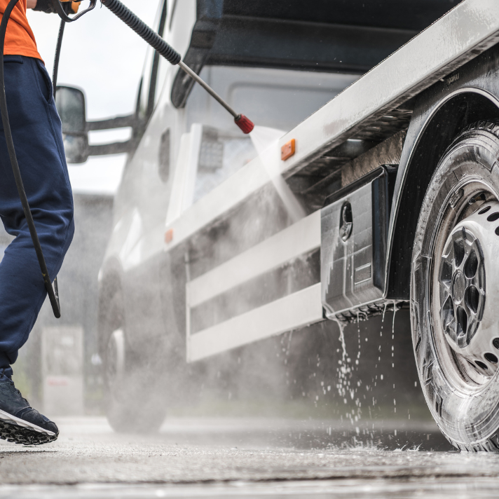 Technician using a pressure washer to clean the side and wheel of a fleet vehicle.