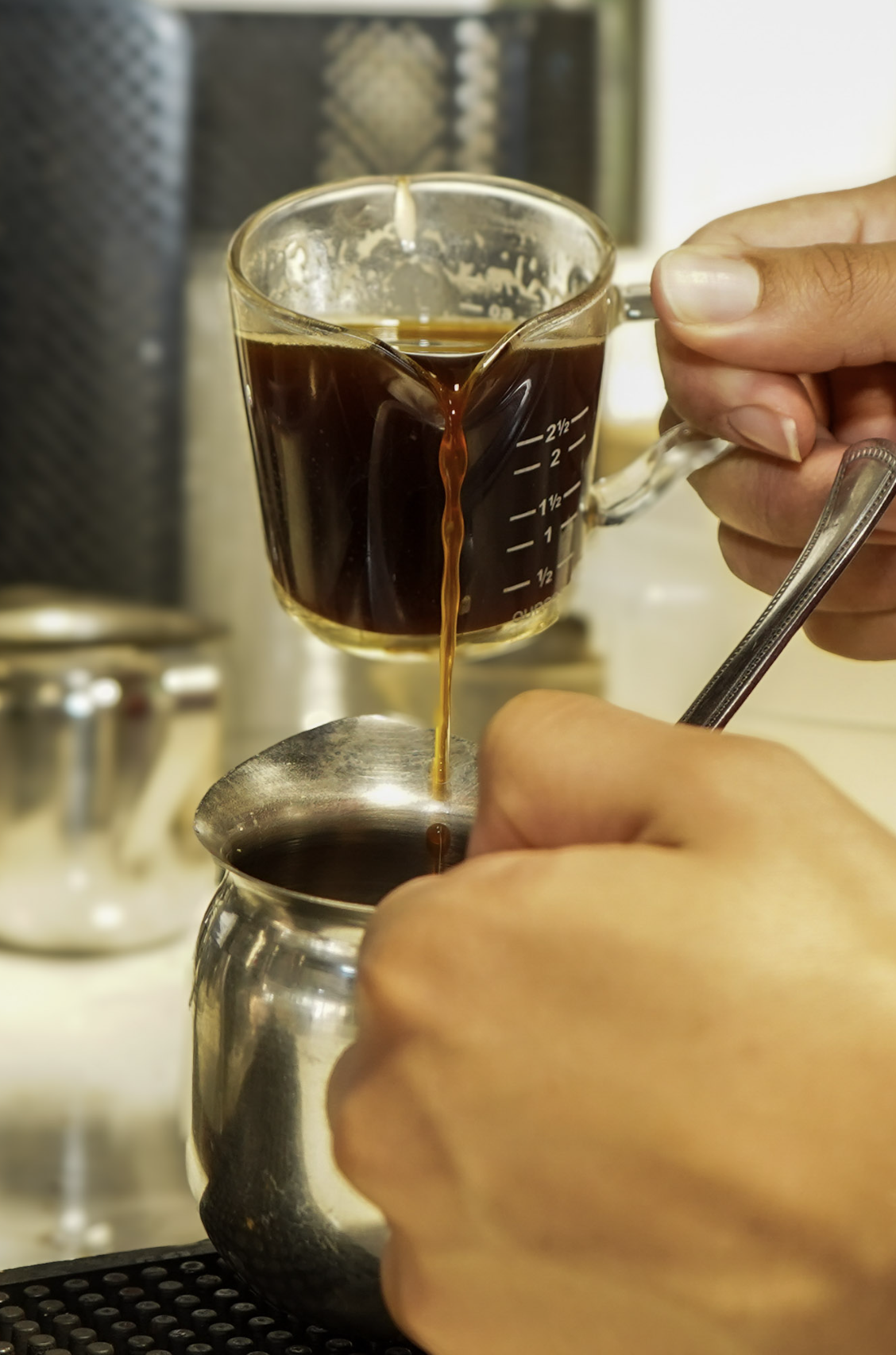 Hands pouring Cuban coffee into a steel pitcher