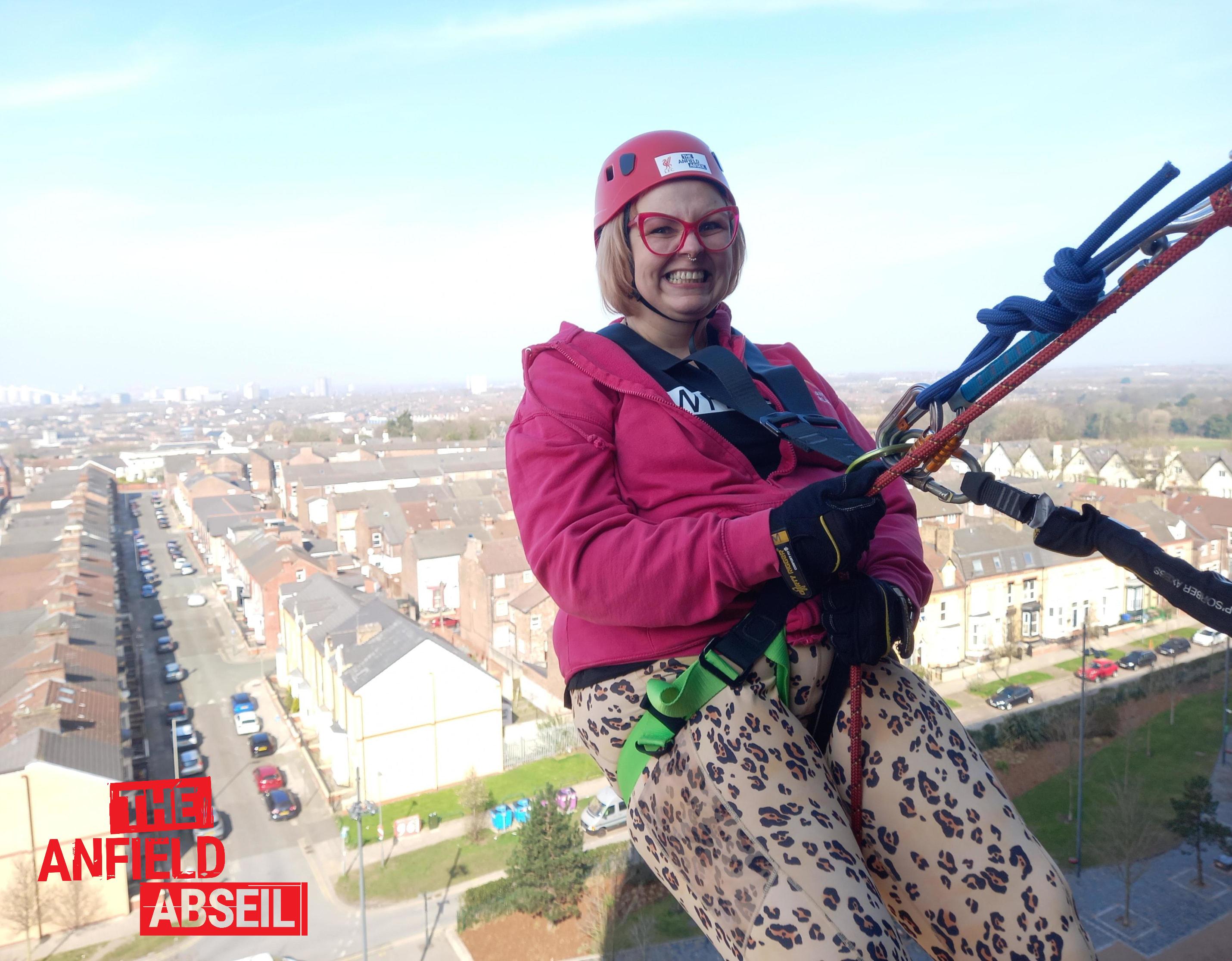Kim Antrobus grinning in a helmet and leopard print leggings while abseiling down the side of Anfield