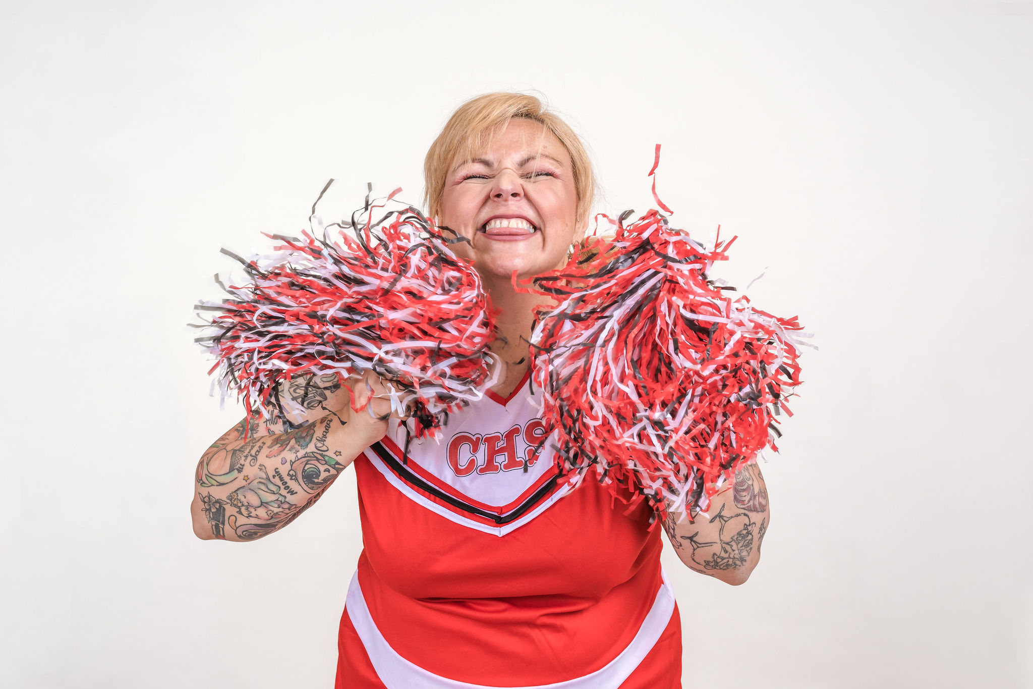 Kim Antrobus in a cheerleader outfit, grinning and holding up red and white pom poms