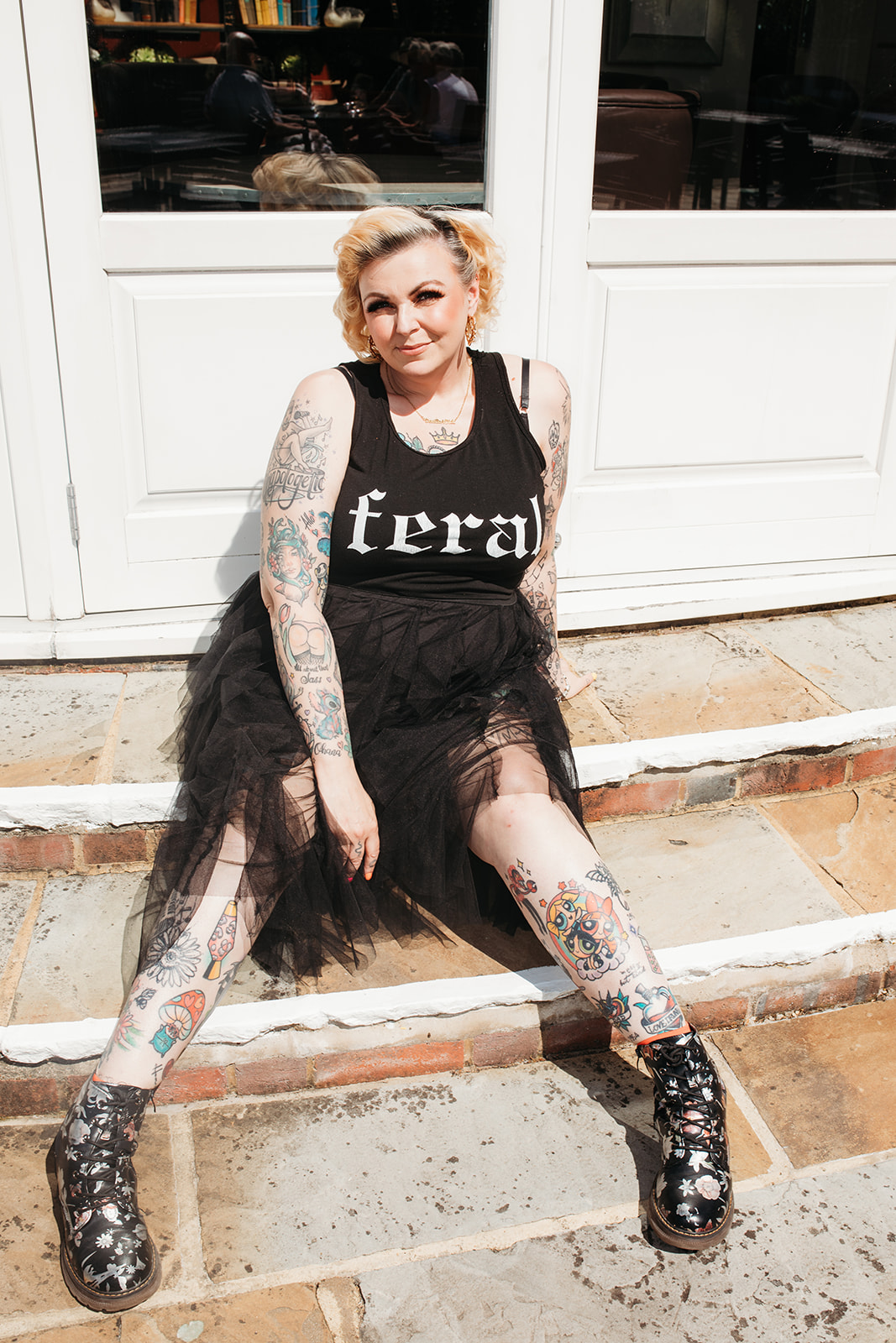 Kim Antrobus sitting on stone steps in a feral t-shirt and chunky boots