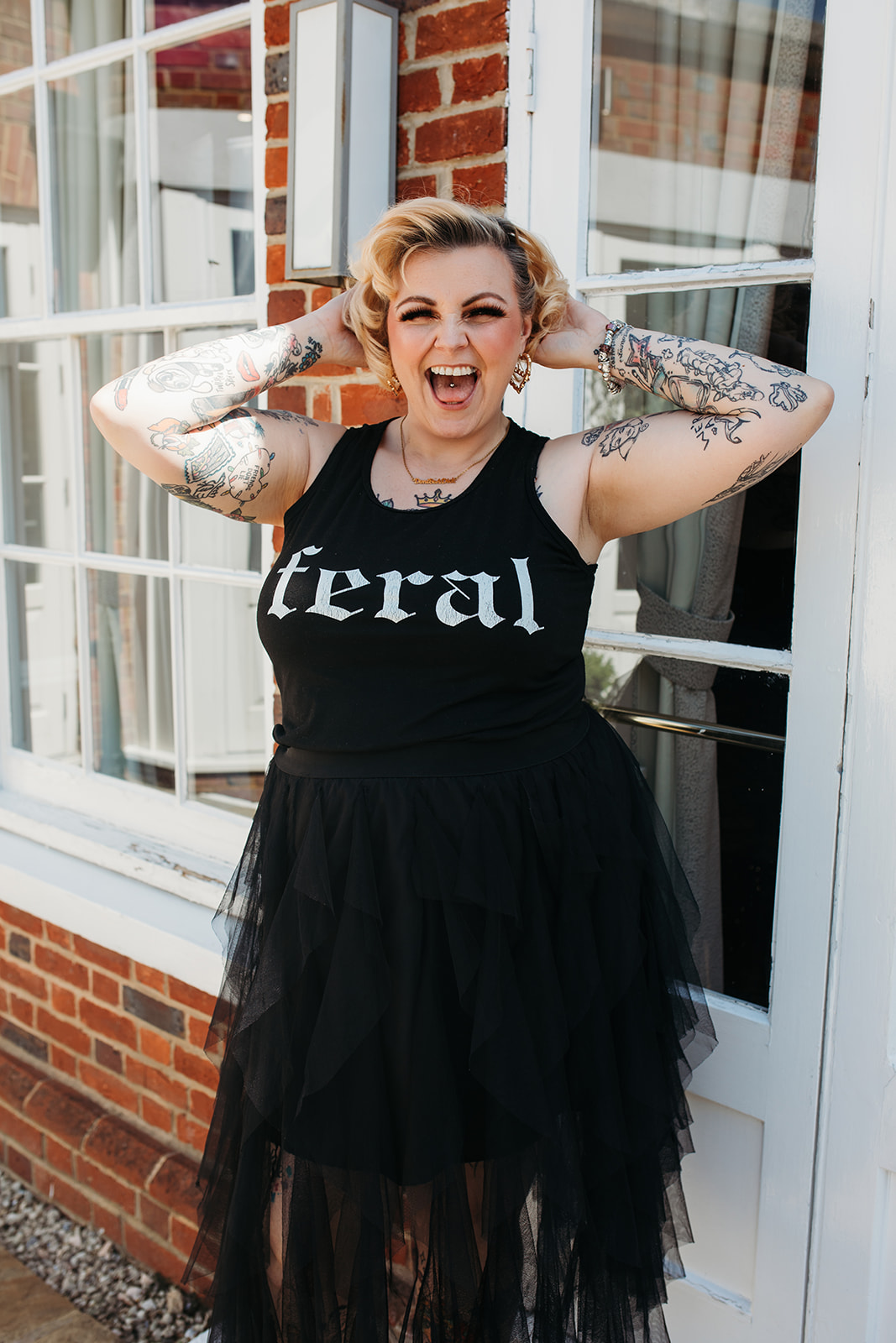 Kim Antrobus in a feral t-shirt and tulle skirt, arms up and laughing