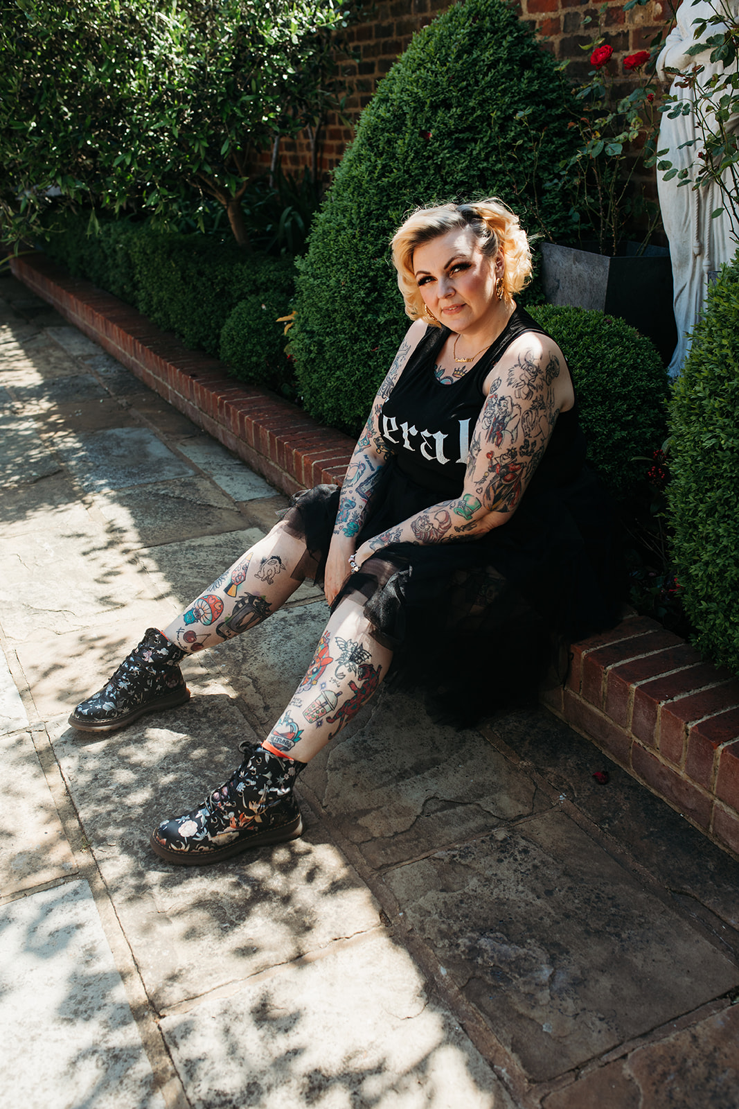 Kim Antrobus sitting on a garden wall in a feral t-shirt and tattoos on show