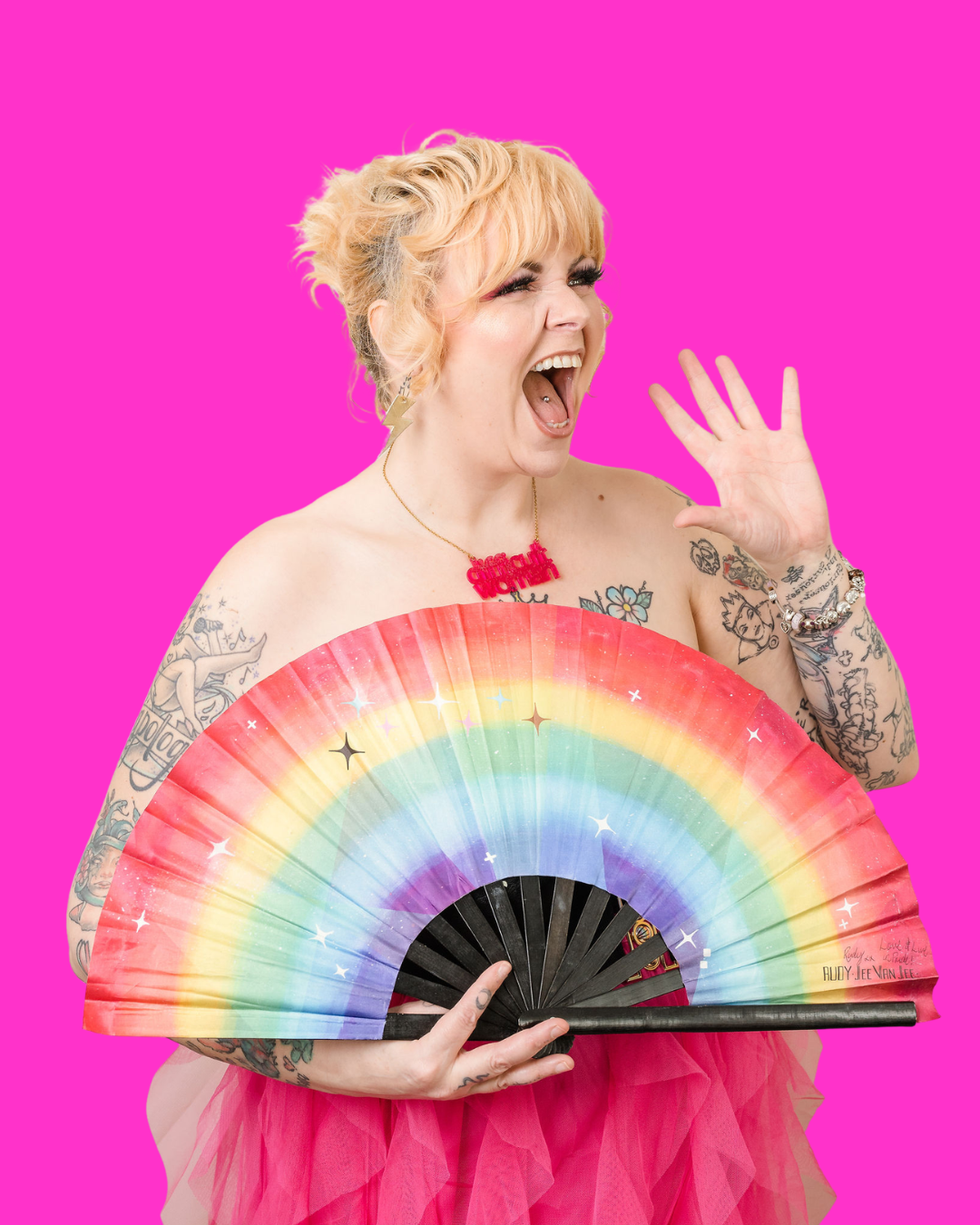Kim Antrobus waving and laughing behind a rainbow fan