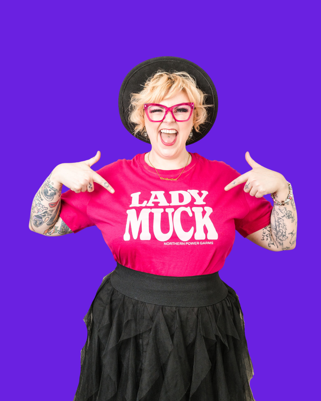 Kim Antrobus grinning and pointing at herself in pink glasses