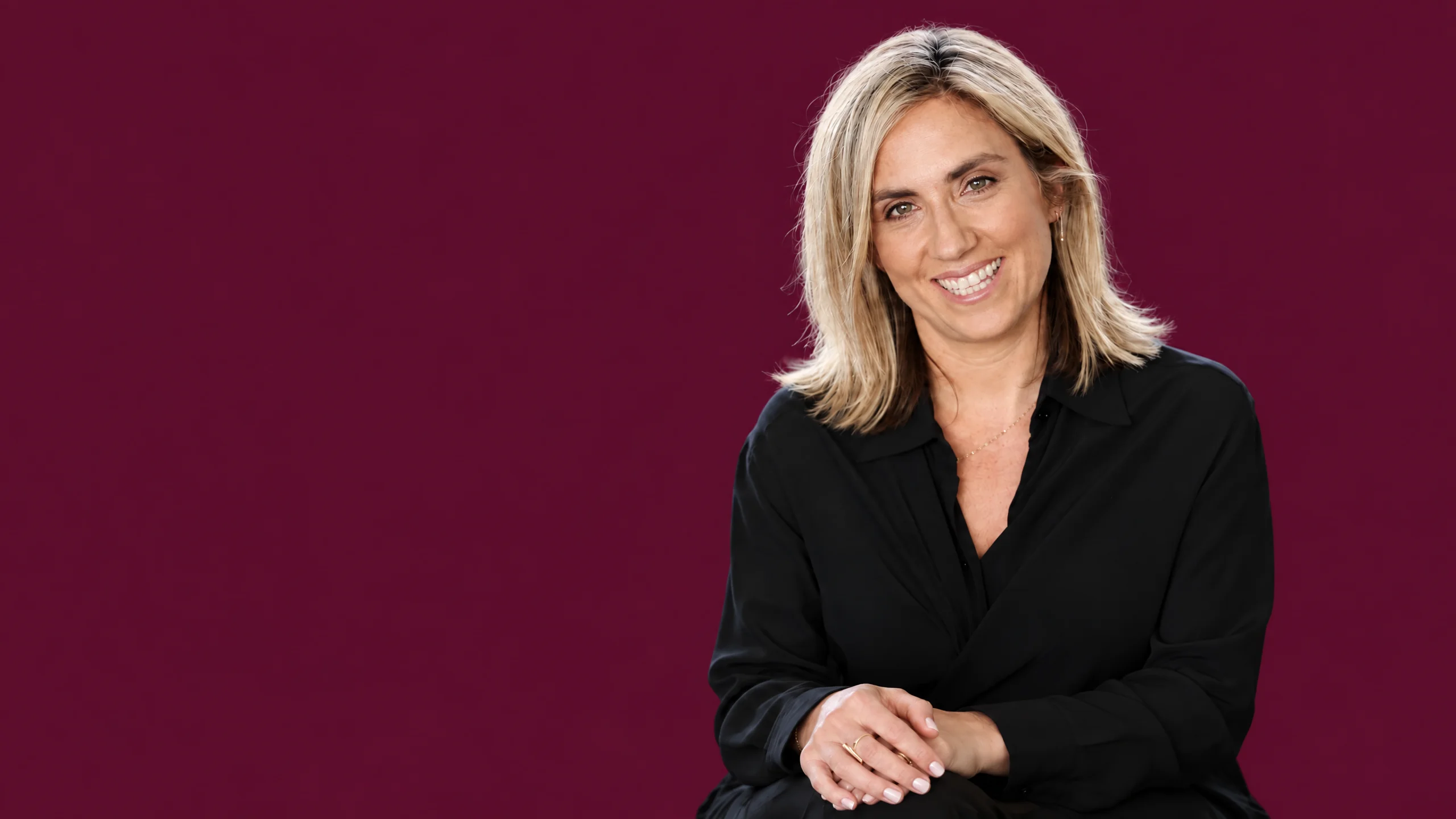 Monique Etkind seated and smiling in a black shirt against a beet backdrop